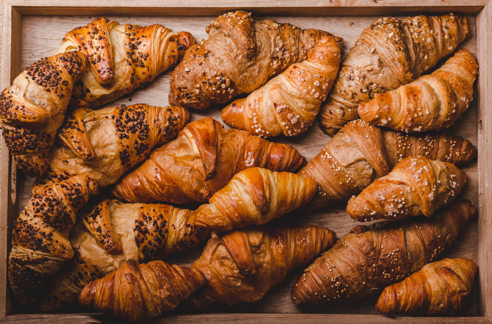 From above of assorted golden baked croissants with different toppings on wooden board.